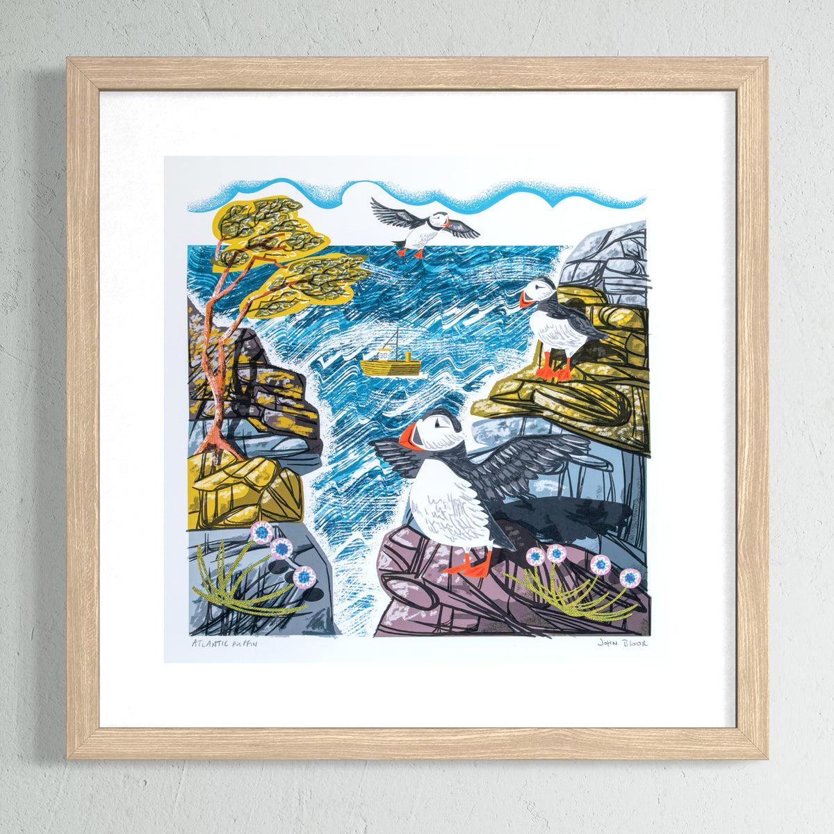 Framed artwork of puffins on a rocky coastline with trees and a boat.