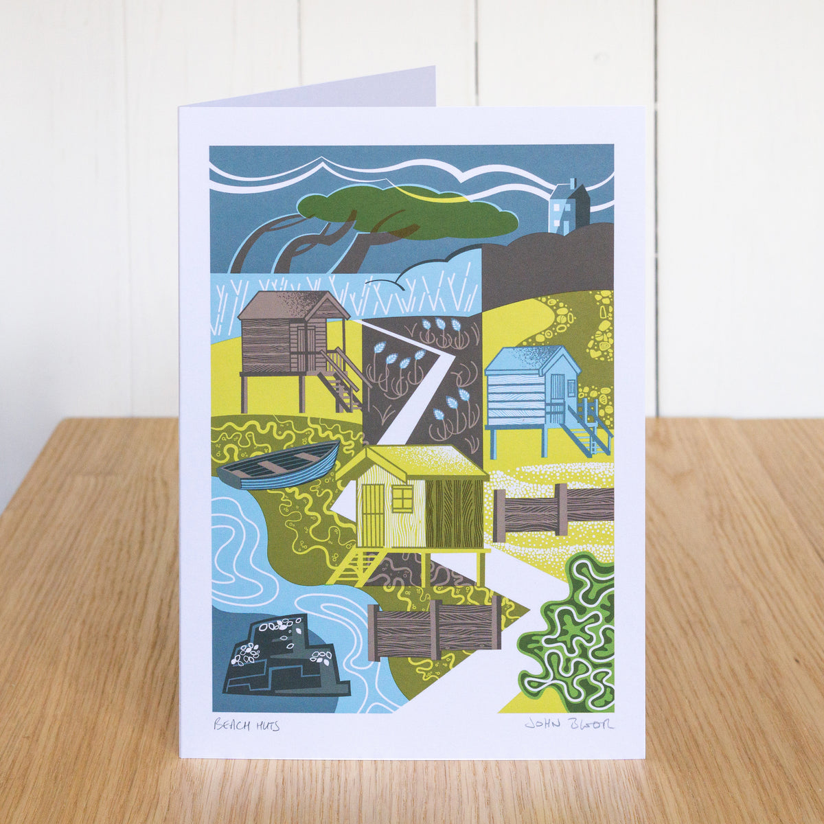 Beach Huts greetings card. It depicts beach huts in an abstract illustration, with trees, a house, sea kale and rocks.