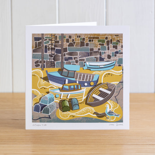 Between Tides greetings card depicting a view of Mousehole Harbour floor with the tide out, showing boats, lobster pots, a gull and the harbour wall. 