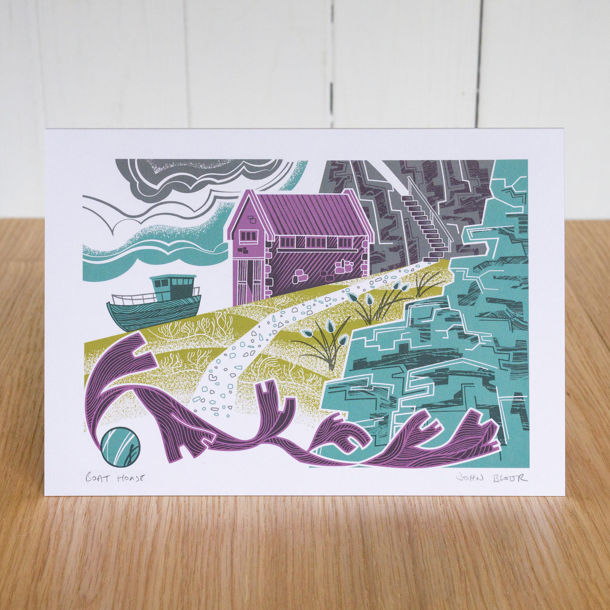 Boat House greetings card. It depicts a boat house on a slipway, with a boat, seaweed and cliffs. 