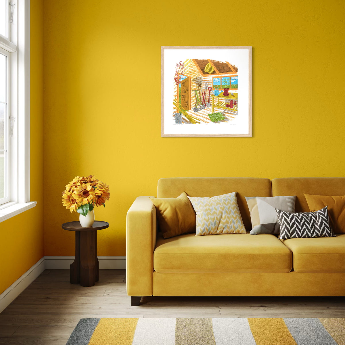 Corner of the Shed screenprint. It depicts the interior of a shed in yellow, orange and brown, showing gardening tools, pots, watering can, mower, and seedlings. Shown in an oak frame on a bright yellow wall with a yellow sofa below.