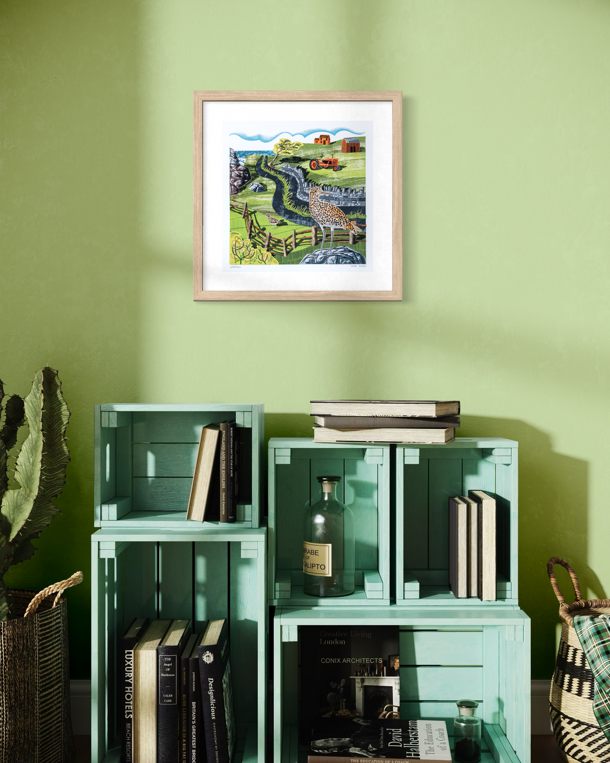 Curlew, British coastal bird, print in an oak frame on a green wall. The print shows a Curlew standing on a rock in the foreground, and one standing on grass. In the background is a farm.