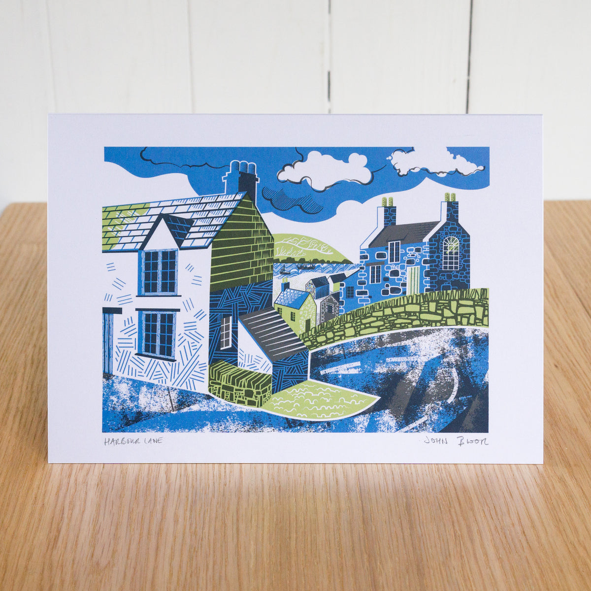Harbour Lane greetings card depicting a road going down a hill into a harbour with houses on either side. 