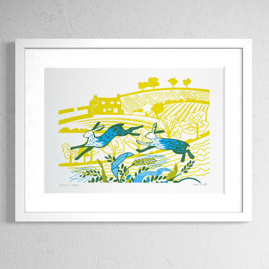 Leaping Hares screenprint in yellow and cyan showing two hares leaping over grasses and wheat in front of a countryside scene. Shown in a white frame.