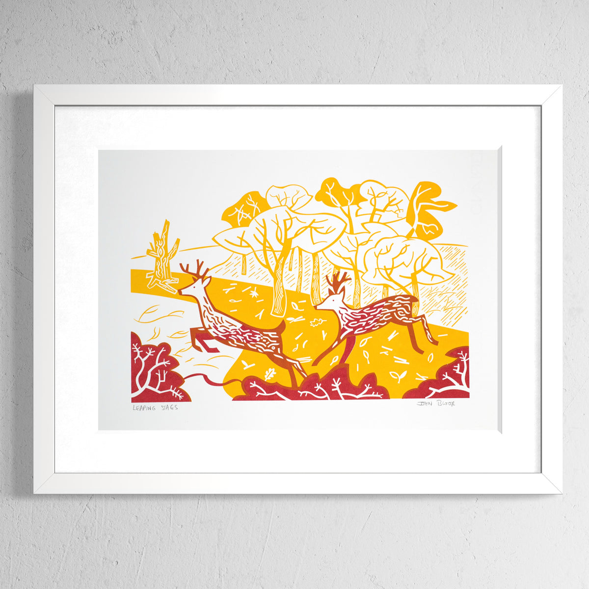 Leaping Stags screenprint in orange and red showing two stags leaping over bushes in front of woods. Shown in a white frame.