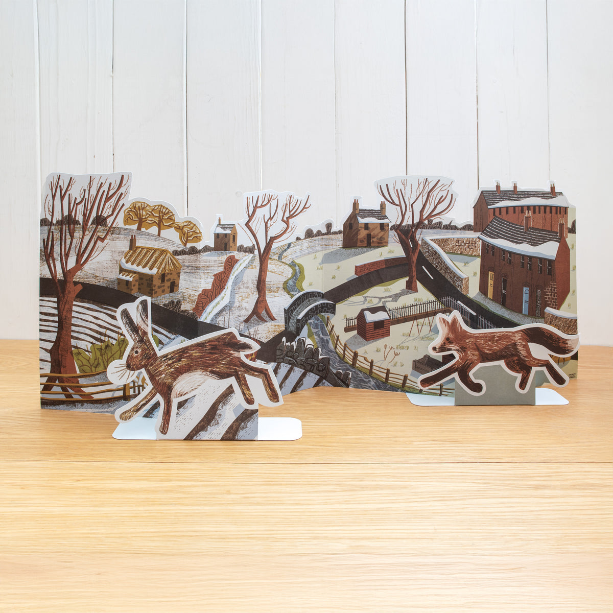 This is a stand-up, concertina fold, Winter scene. It features an urban moving into a rural scene with a river, allotment, trees, houses, sheds and hedgerows.

It features two separate stand up animals; a fox and a hare.