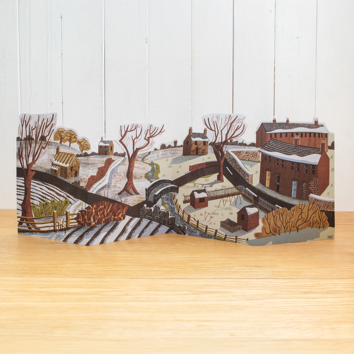 This is a stand-up, concertina fold, Winter scene. It features an urban moving into a rural scene with a river, allotment, trees, houses, sheds and hedgerows.