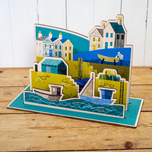 Wooden Harbour hand printed scene. It shows a harbour scene with sea and boats in the foreground, a harbour wall with ladder, lobster pots and a hut, behind is a fisherman working on a boat and houses.