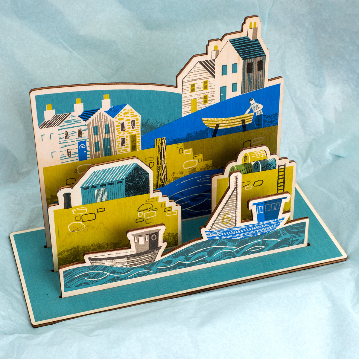 Wooden Harbour hand printed scene. It shows a harbour scene with sea and boats in the foreground, a harbour wall with ladder, lobster pots and a hut, behind is a fisherman working on a boat and houses.