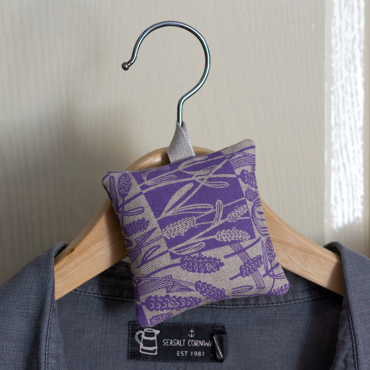 A singe square lavender bag with hanging loop, hanging on a clothes hanger.