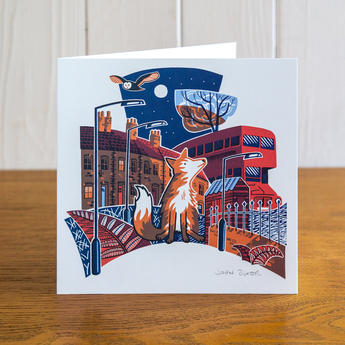 Majestic Animals Fox card. It depicts a fox sitting between houses, a red bus, railings, a shed and ferns. Above is an owl. 