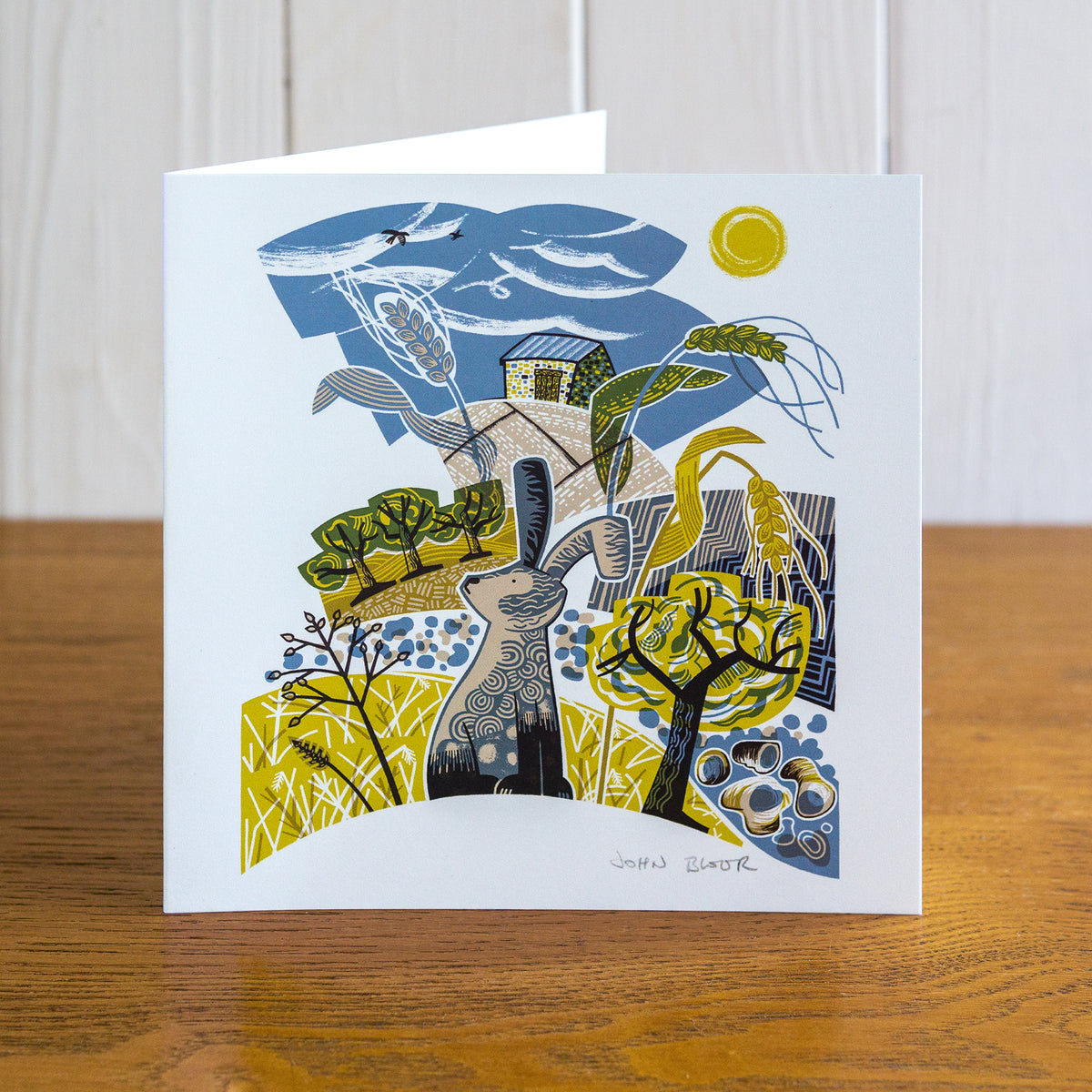 Majestic Animals Hare card. It depicts a hare standing in front of fields of wheat and pebbles. Behind is a farm building. 