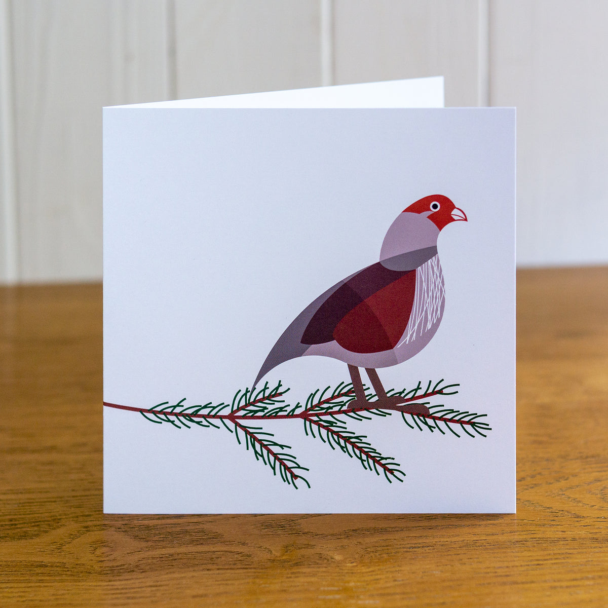 Partridge Christmas card depicting a partridge standing on a fir tree branch.