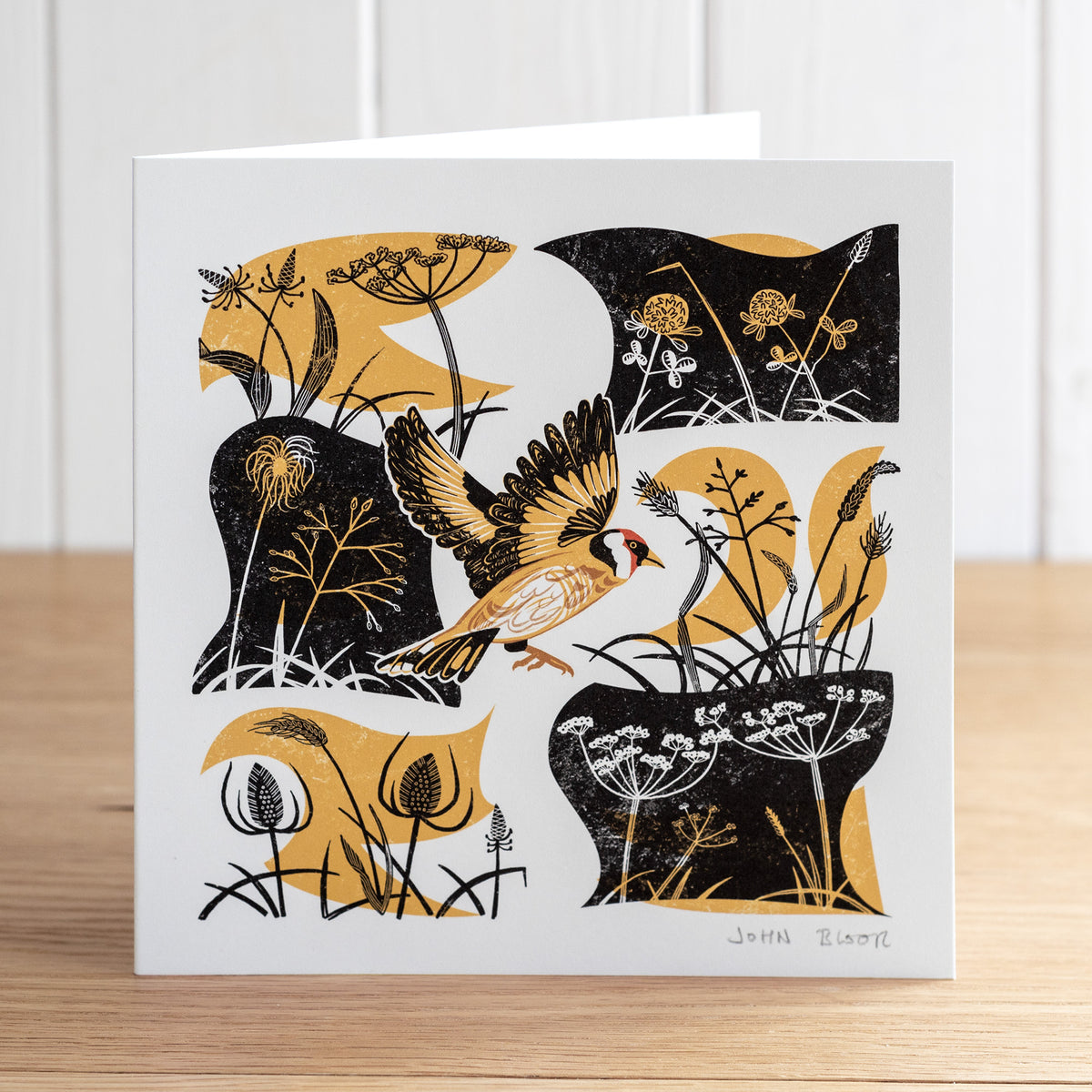 Take Flight Goldfinch greetings card. This card depicts a goldfinch flying amongst grasses and seed heads.
